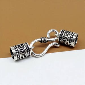 May include: Silver-toned metal clasp with a hook and two decorative end caps. The end caps have a geometric pattern.