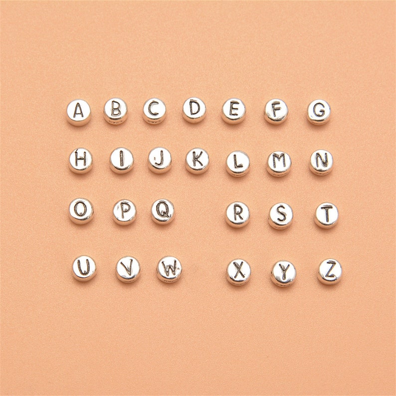 May include: Silver alphabet letter beads, A through Z, arranged in rows on a light orange background.