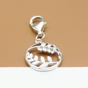 May include: Silver charm with a circle design featuring two intertwined branches of leaves. The charm has a lobster claw clasp.