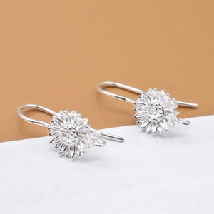 May include: A pair of silver sunflower dangle earrings with a hook closure.