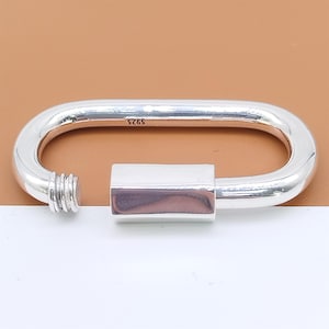May include: A silver-colored, oval-shaped clasp with a screw-on end and a rectangular closure. The clasp is made of a shiny metal and has the number "925" stamped on it.