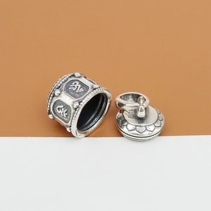 Puede incluir: Encanto de plata con un dise&ntilde;o detallado que presenta un recipiente redondo abierto con una tapa. El recipiente tiene un patr&oacute;n decorativo y la tapa tiene un dise&ntilde;o floral. El encanto tiene un bucle para sujetarlo a una pulsera o collar.