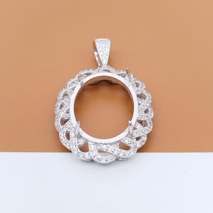 May include: A silver pendant setting with an oval centre and an openwork design. The setting is encrusted with small, clear stones and has a bail for a chain.