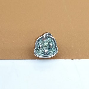 Puede incluir: Un amuleto de plata con forma de animal de dibujos animados con un acabado de esmalte verde y azul.