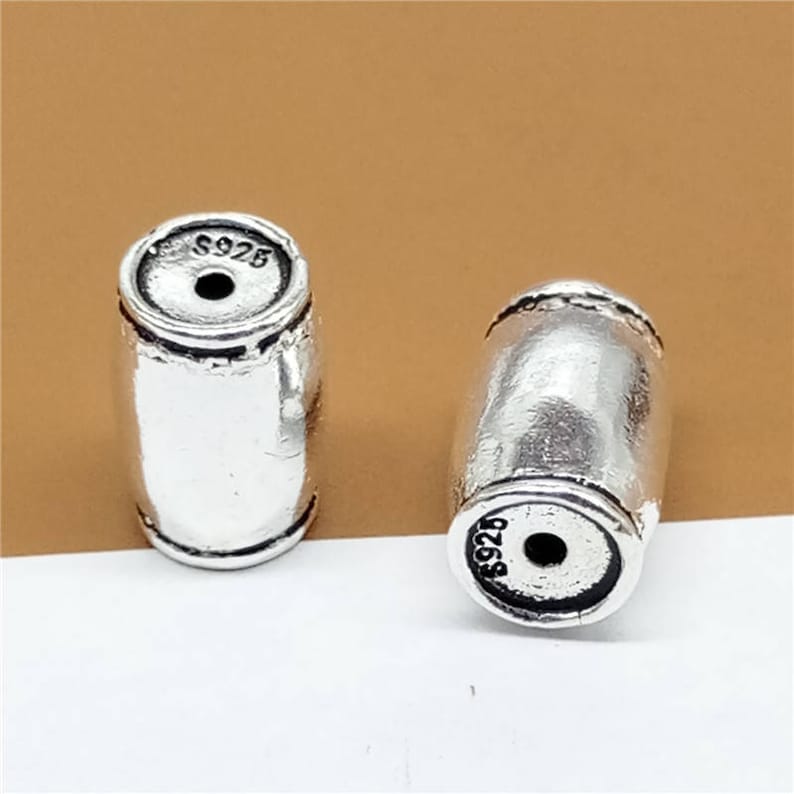 K&ouml;nnte beinhalten: Zwei silberfarbene, zylindrische Perlen aus Metall mit der Gravur "S925" auf jeder Perle.
