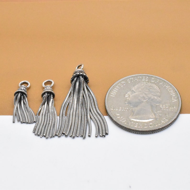 May include: Three silver tassel charms of varying sizes, the largest is about the size of a US quarter.
