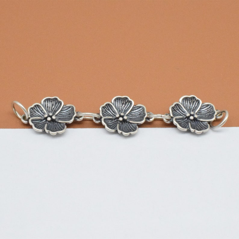 May include: A silver chain with three flower-shaped charms. The flowers are detailed and have a black oxidized finish.