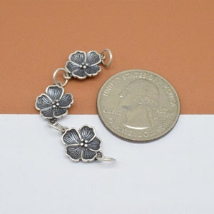 May include: A silver charm bracelet with three flower charms. The charms are detailed with a textured surface and are about the size of a US quarter.