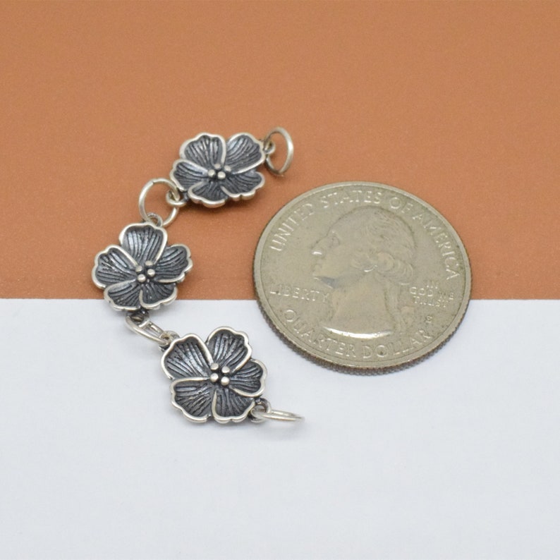 May include: A silver charm bracelet with three flower charms. The charms are detailed with a textured surface and are about the size of a US quarter.