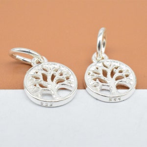 Op de afbeelding: Twee zilveren boom des levens bedels met een rond ontwerp en een lus om aan een armband of ketting te bevestigen. De bedels zijn gemarkeerd met "925" aan de achterkant.