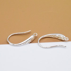 May include: Two silver earring hooks with a decorative design. The hooks are made of metal and have a shiny finish.