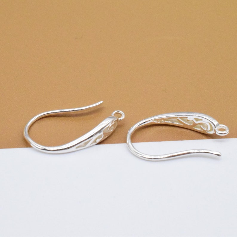 May include: Two silver earring hooks with a decorative design. The hooks are made of metal and have a shiny finish.