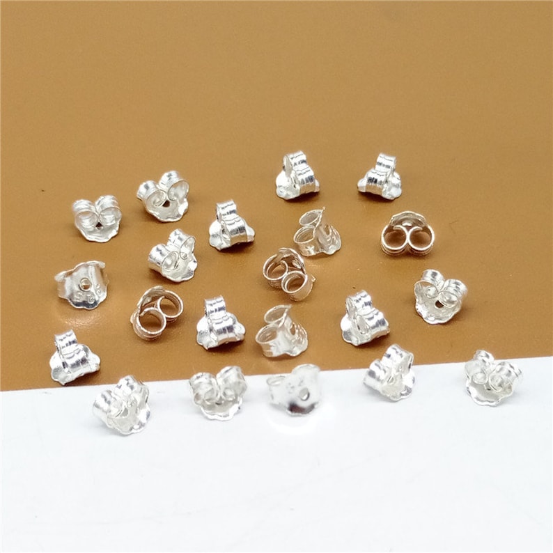 May include: A collection of silver earring backs, also known as earring stoppers, for securing earrings. The backs are designed with a three-pronged shape for a secure fit.