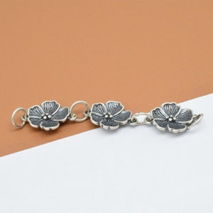 May include: Silver charm bracelet with three flower-shaped charms connected by a chain. The flowers are silver with a dark gray finish.