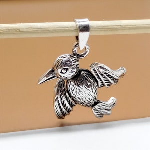 May include: Silver charm pendant featuring a detailed bird design with wings outstretched. The bird has a small beak and a textured surface.