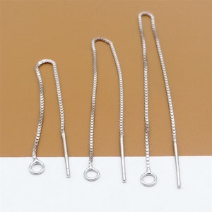 May include: Three silver chain earring extenders of varying lengths. The extenders are made of a delicate chain with a small loop at the top and a straight, thin wire at the bottom.