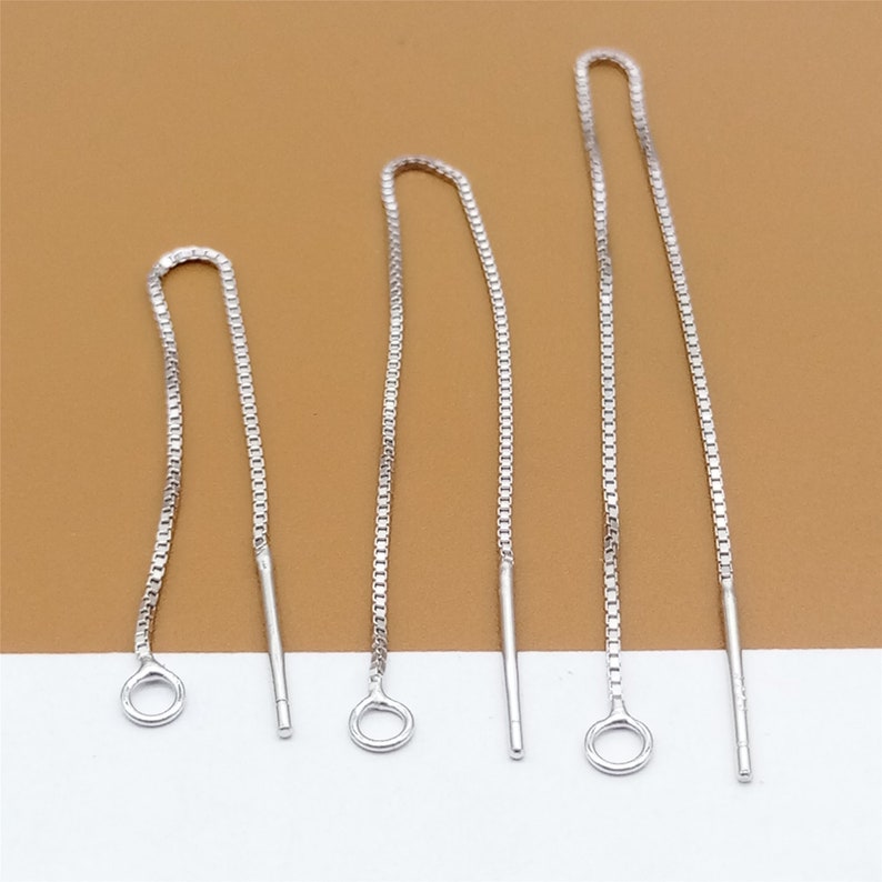 May include: Three silver chain earring extenders of varying lengths. The extenders are made of a delicate chain with a small loop at the top and a straight, thin wire at the bottom.