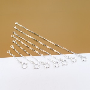 Puede incluir: Seis cadenas de extensión plateadas de diferentes longitudes, cada una con un cierre de langosta.