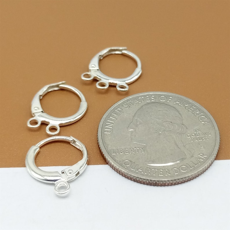 May include: Three silver earring hoops with a jump ring and three small loops on each hoop. The hoops are about the size of a US quarter.