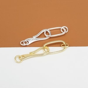 May include: Two metal clasps, one silver and one gold, with a hook and oval ring design. Both clasps have a small inscription on the side, "S925" and "S925".