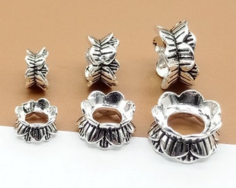 May include: Five silver metal bead caps with a decorative floral design. The bead caps are different sizes and are arranged in a row on a brown surface.