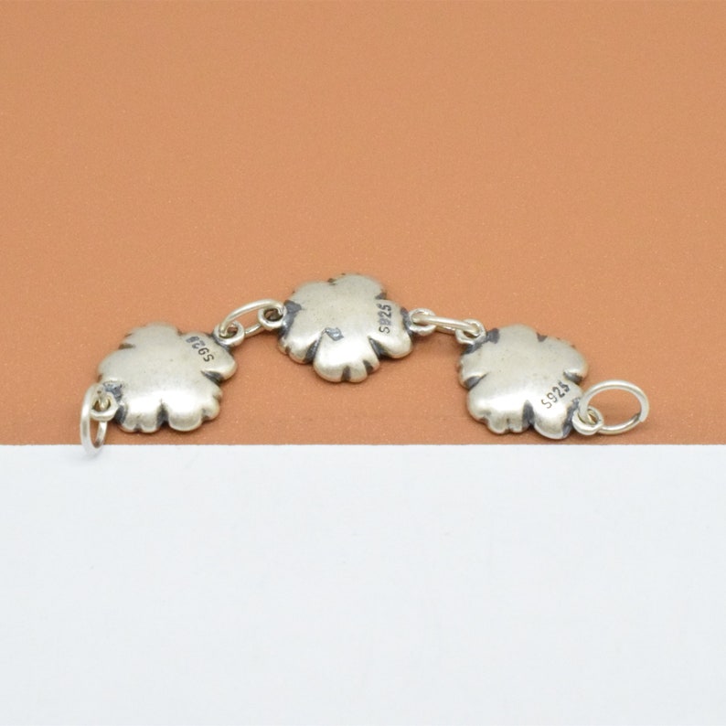 May include: A silver charm bracelet with three clover-shaped charms. Each charm has the number "5925" engraved on the back.