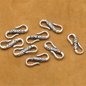 May include: Eight silver-toned metal clasps with intricate designs. Each clasp has a hook and loop closure.