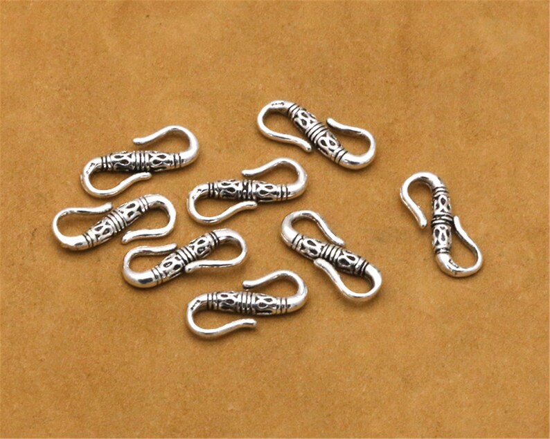 May include: Eight silver-toned metal clasps with intricate designs. Each clasp has a hook and loop closure.