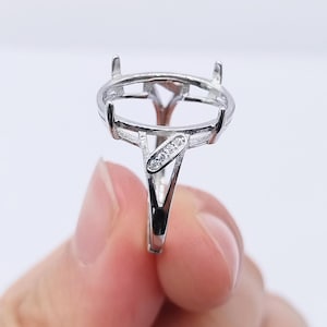 Puede incluir: Un engaste de anillo plateado con un bisel ovalado y un vástago en forma de V. El anillo presenta pequeñas piedras preciosas transparentes engastadas en la banda. El engaste está diseñado para sujetar una piedra preciosa.