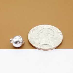 May include: A silver magnetic clasp for jewelry, next to a US quarter for size comparison. The clasp is round and has a smooth surface.