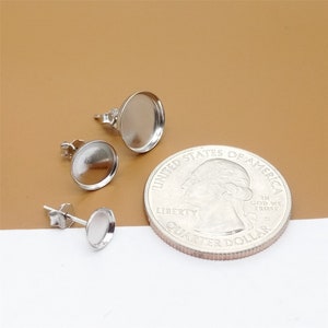 May include: Three silver earring settings with a round, flat, silver base. The earring settings are shown next to a US quarter for size comparison.