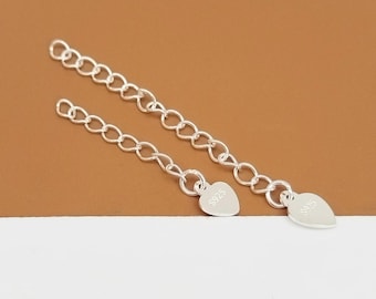 May include: Two silver-colored chain extenders with heart-shaped charms. Each charm is stamped with "S925". The chains are made of small, interconnected oval links. The background is a gradient of brown and white.