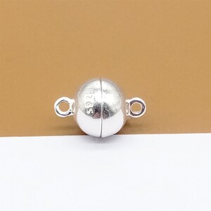 May include: Silver magnetic clasp for jewelry making. The clasp is round and has a smooth, polished finish. It is marked with "S925" on one side.
