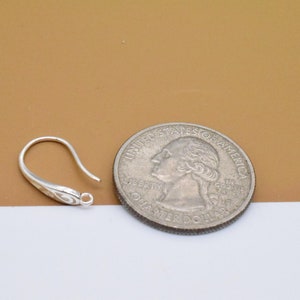 May include: Silver earring hook with a decorative swirl design. The hook is about the size of a US quarter.