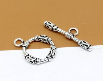 May include: Silver tone toggle clasp with a round, ornate design and a straight, ornate bar.