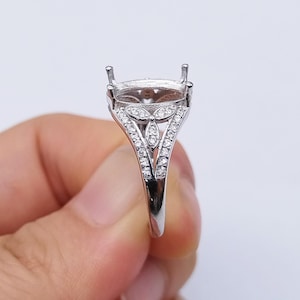 May include: A silver ring setting with a decorative design. The ring features a central setting for a gemstone, flanked by a detailed pattern of small, sparkling stones. The band splits into a decorative design on the sides.