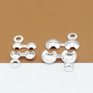 May include: Silver-toned metal bead caps for jewelry making. The caps have a rounded shape with a small hole on each side for threading.