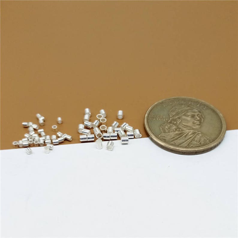 May include: A close-up of a pile of small, silver-colored metal tubes, with a US quarter for scale. The tubes are about the size of a grain of rice.