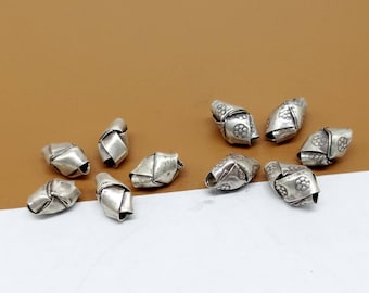 May include: A collection of ten silver-toned metal beads with a knotted design. The beads are all the same size and shape, and they have a slightly textured surface.