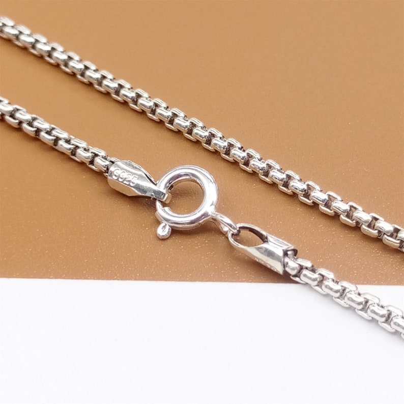 May include: A silver chain necklace with a lobster clasp closure. The chain is made of small, linked circles.