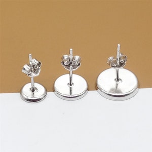 May include: Three silver earring posts with round backings. The posts are different sizes.