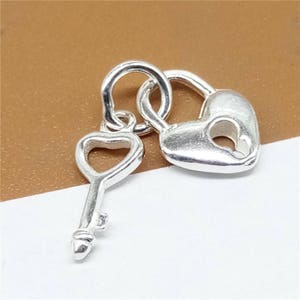 Puede incluir: Encanto de candado y llave de plata en forma de corazón. El candado tiene una cerradura en forma de corazón. La llave también tiene forma de corazón.