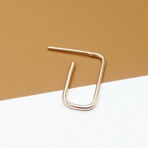 May include: A gold-toned, open hoop earring with a simple, rectangular shape.