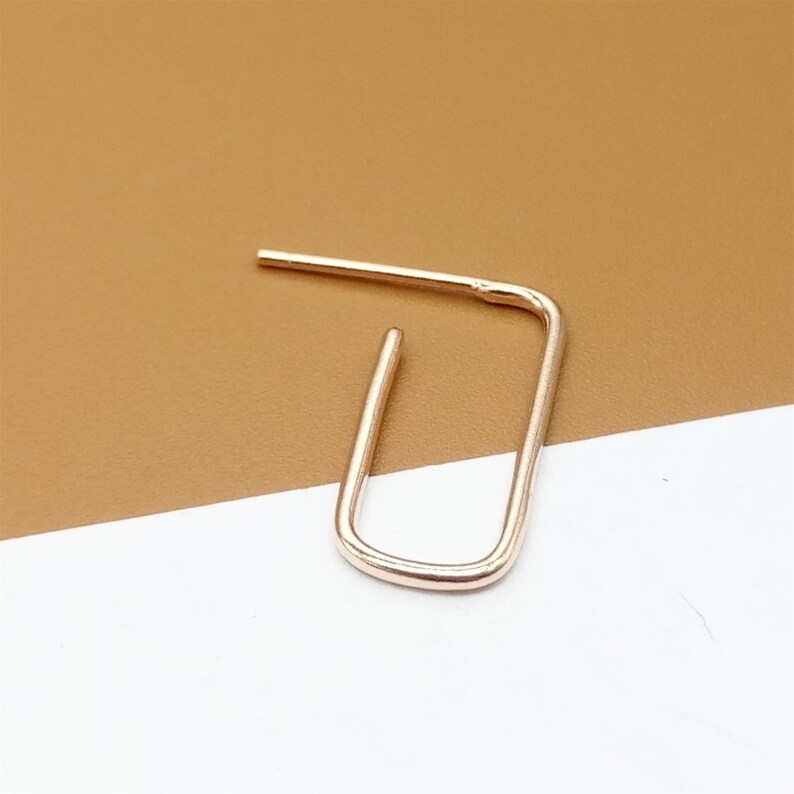 May include: A gold-toned, open hoop earring with a simple, rectangular shape.