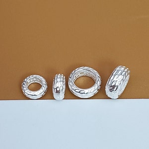 May include: Four silver rings with a textured surface. The rings are all the same size and shape, but they are arranged in a row so that they are slightly offset from each other.