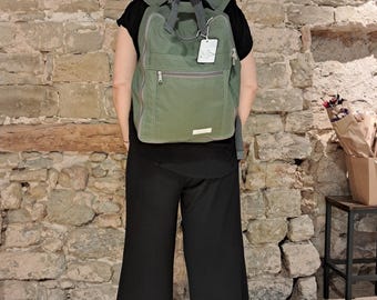 Puede incluir: Una mochila de lona verde con un bolsillo frontal con cremallera y una pequeña etiqueta que dice "Little Green"