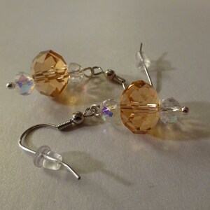 May include: A pair of dangle earrings with a large amber-colored crystal bead and smaller clear crystal beads. The earrings are made with silver-toned metal.