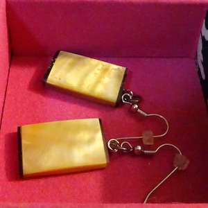 May include: A pair of earrings with a rectangular, iridescent, yellow-gold shell design. The earrings have silver hooks and small, clear, crystal-like accents.