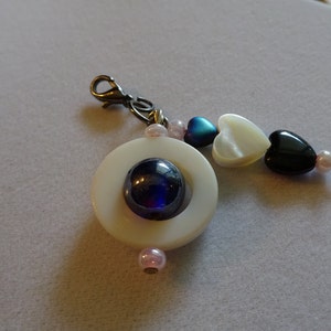 May include: A white circle charm with a blue iridescent center, attached to a silver clasp and a string of pink and white heart-shaped beads.