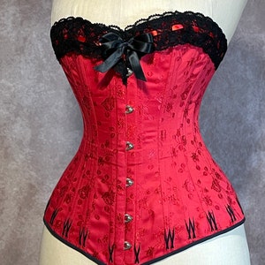 May include: A red corset with black lace trim and a black satin bow. The corset has a floral pattern and is made of a satin-like fabric.